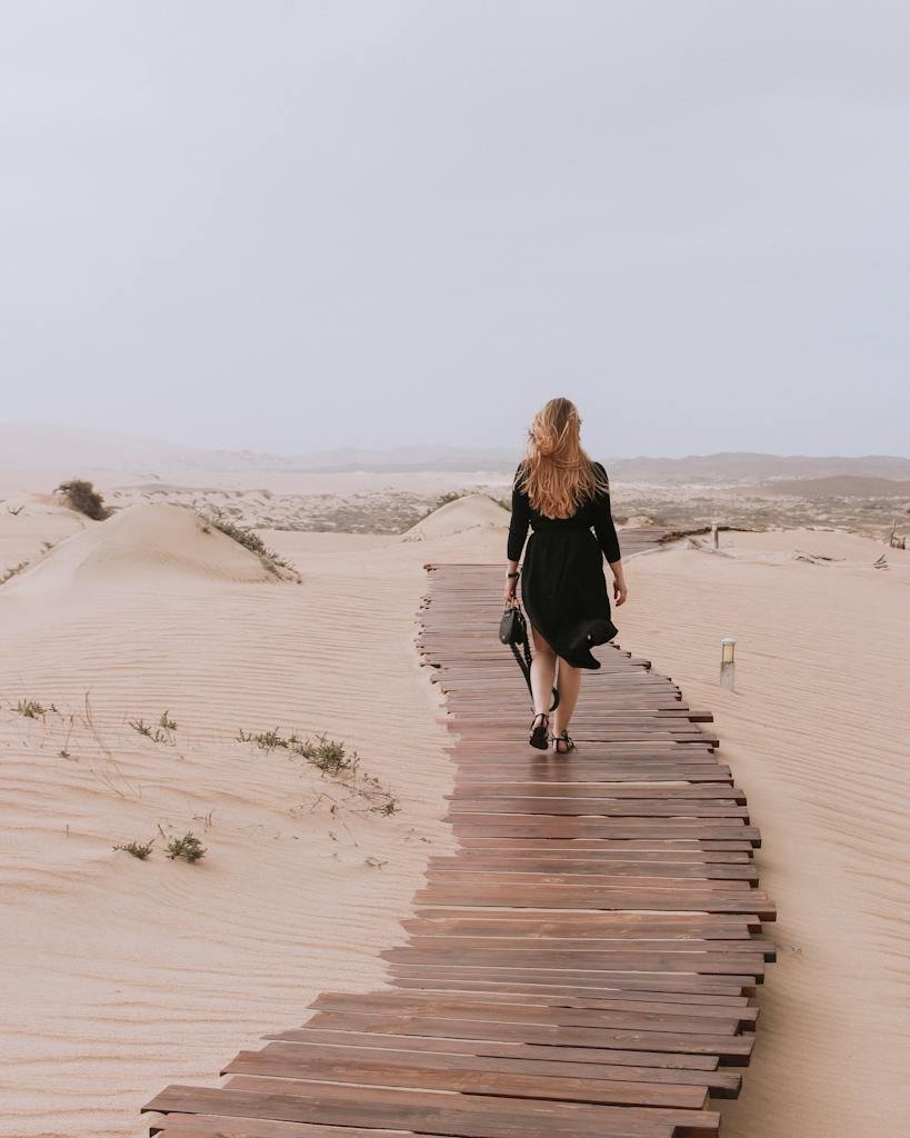 A Woman Walking Alone on a Wooden Pathway on a Desert